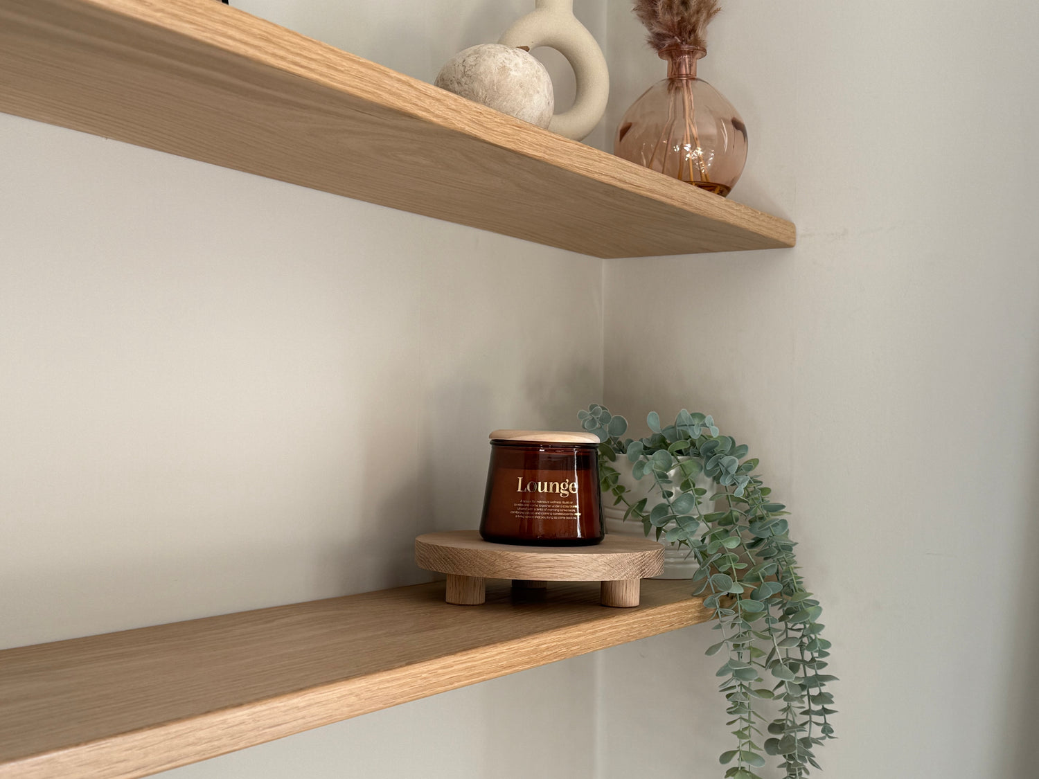 Candle on a wooden riser shelf with decorative items and plants.