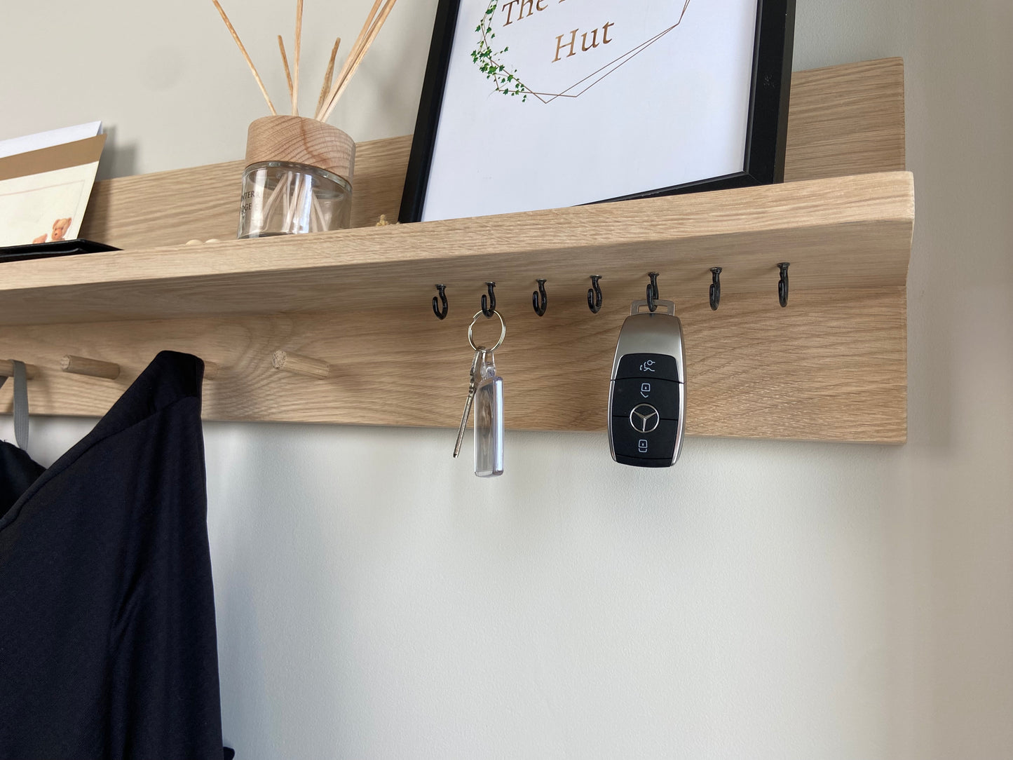 Close up of oak organiser shelf with wooden pegs and hooks wall mounted displaying keys and decorative items.