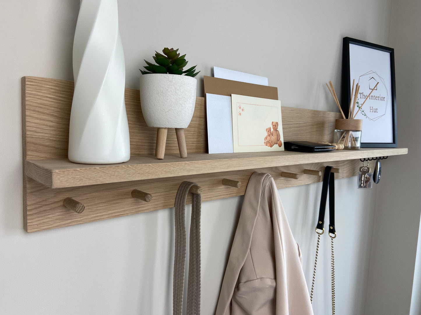 Oak organiser shelf with wooden pegs and hooks wall mounted displaying decorative items.