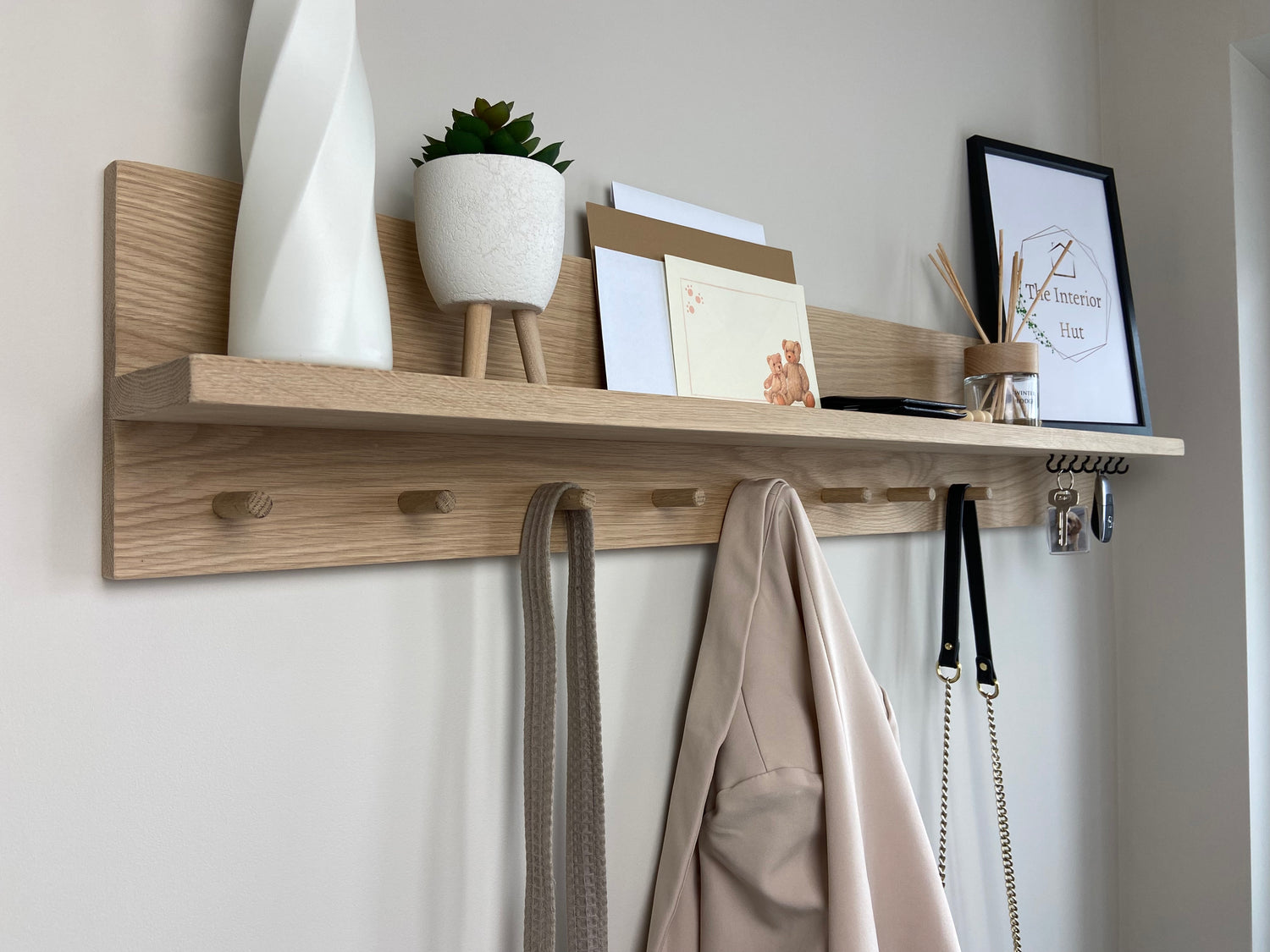 Oak organiser shelf with wooden pegs and hooks wall mounted displaying decorative items.