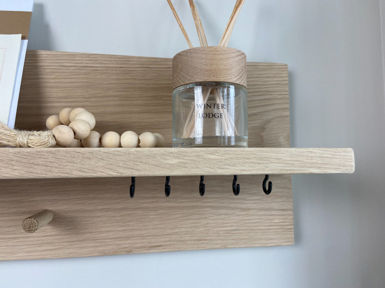 Close up of oak organiser shelf showing hooks wall mounted displaying decorative items.