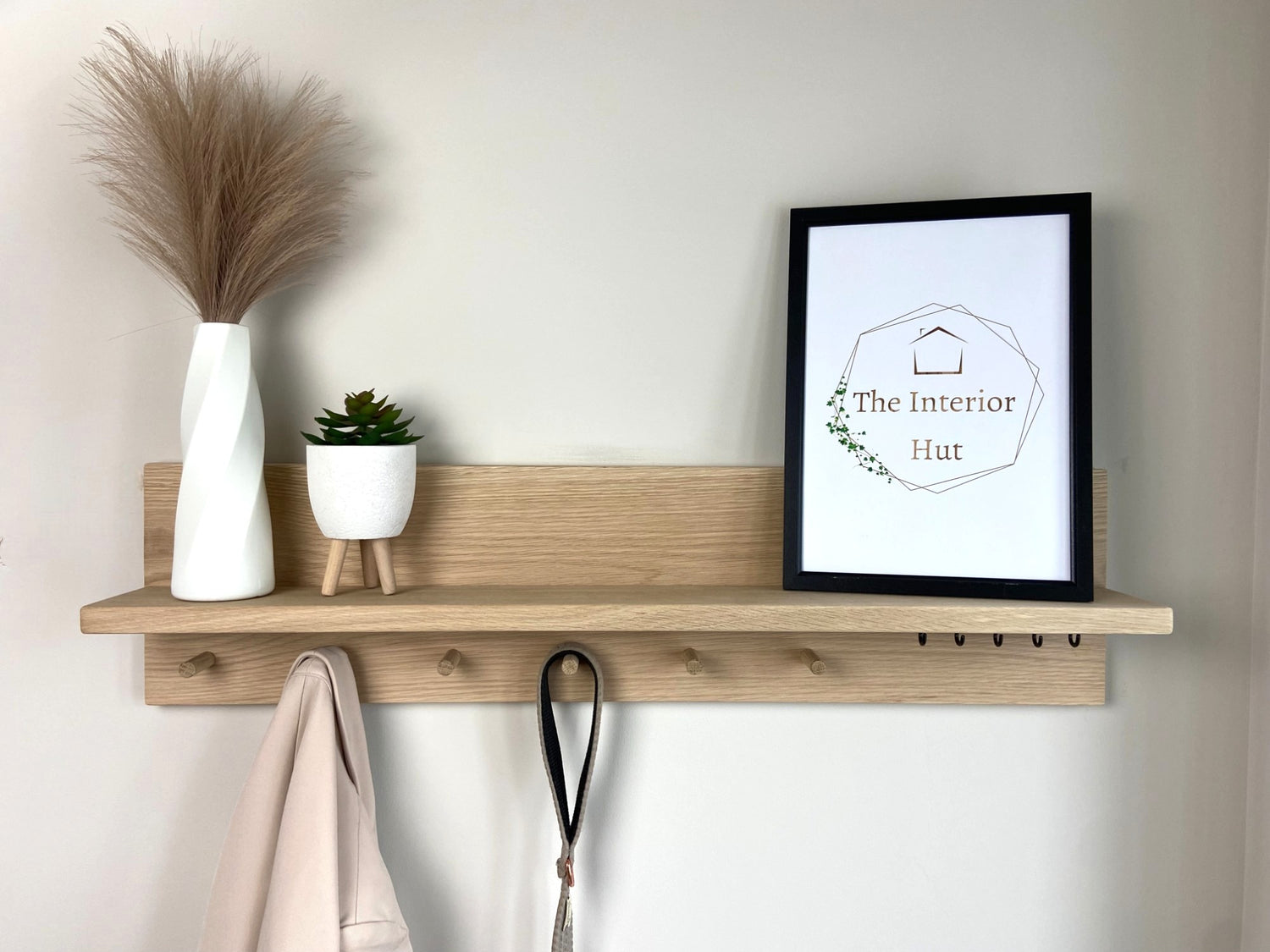 Handcrafted oak organiser shelf with wooden pegs and hooks displaying decorative items mounted to a wall.