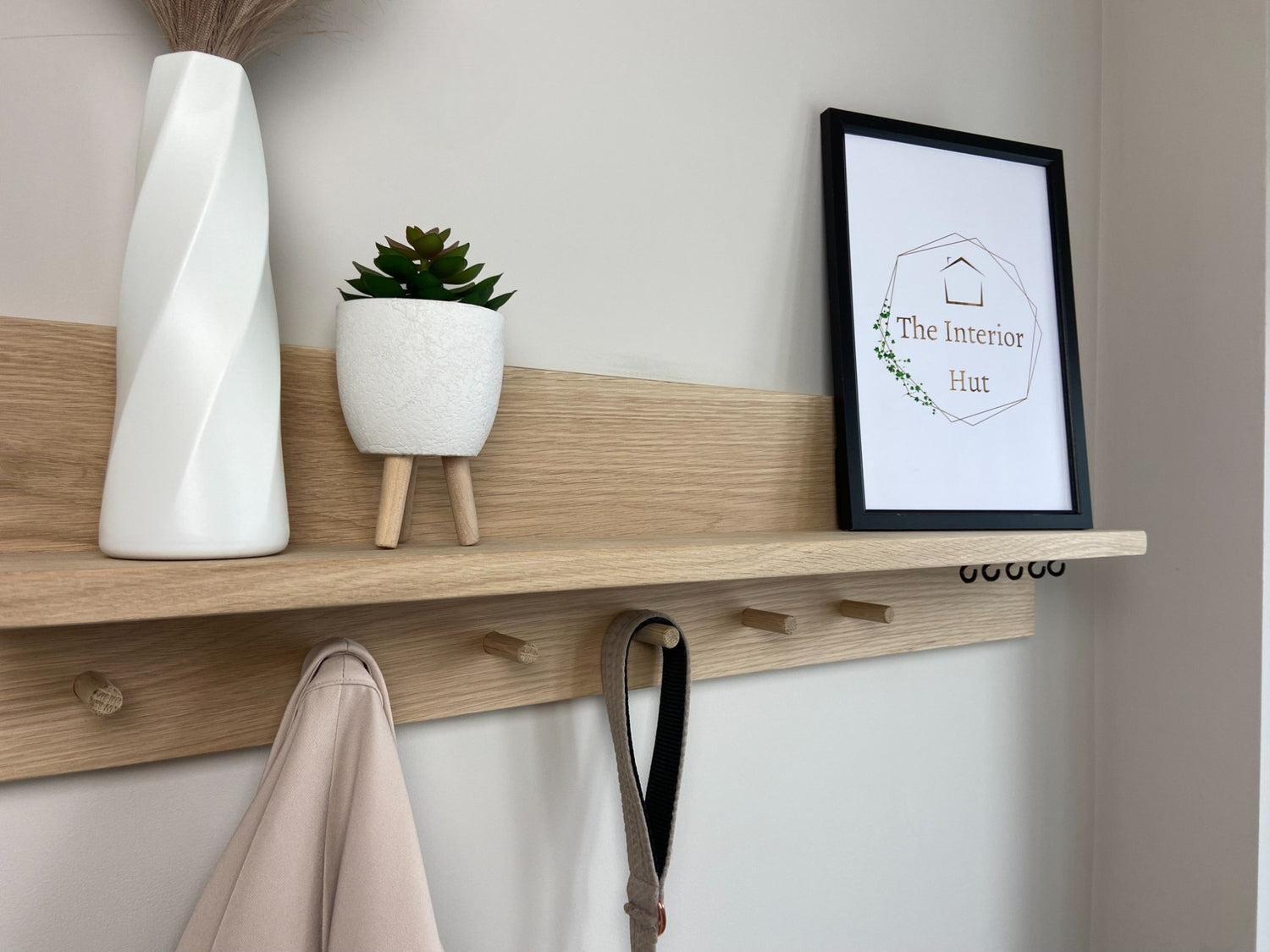 Close up of oak organiser shelf with wooden pegs and hooks wall mounted displaying decorative items.