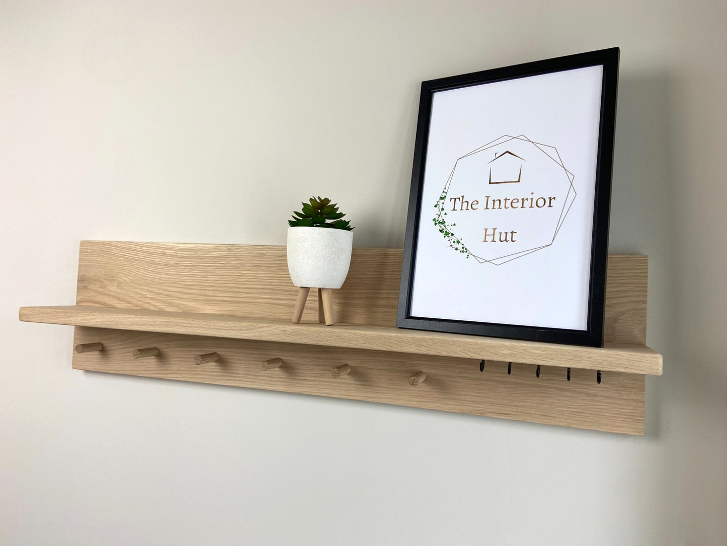 Handcrafted oak organiser shelf with wooden pegs and hooks displaying a plant and picture frame