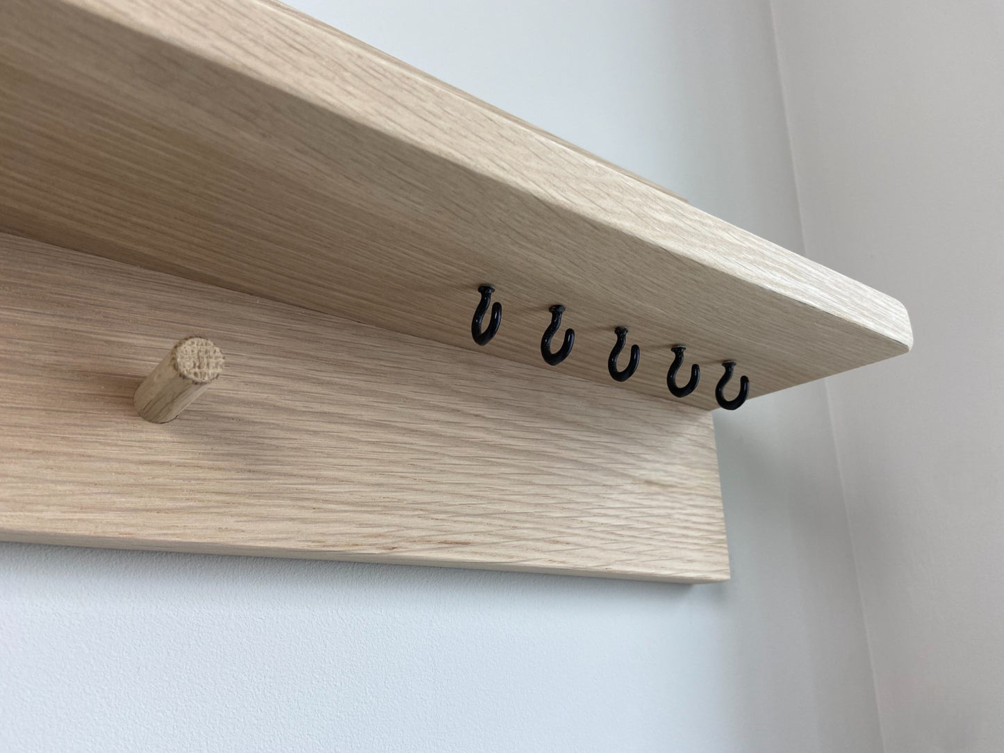 Close up of handcrafted oak organiser shelf clearly showing black hooks  mounted to a wall in an entryway. 