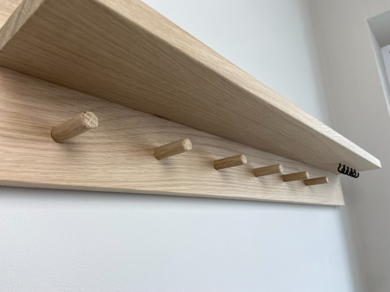 Close up of handcrafted oak organiser shelf clearly showing wooden pegs and hooks  mounted to a wall in an entryway. 