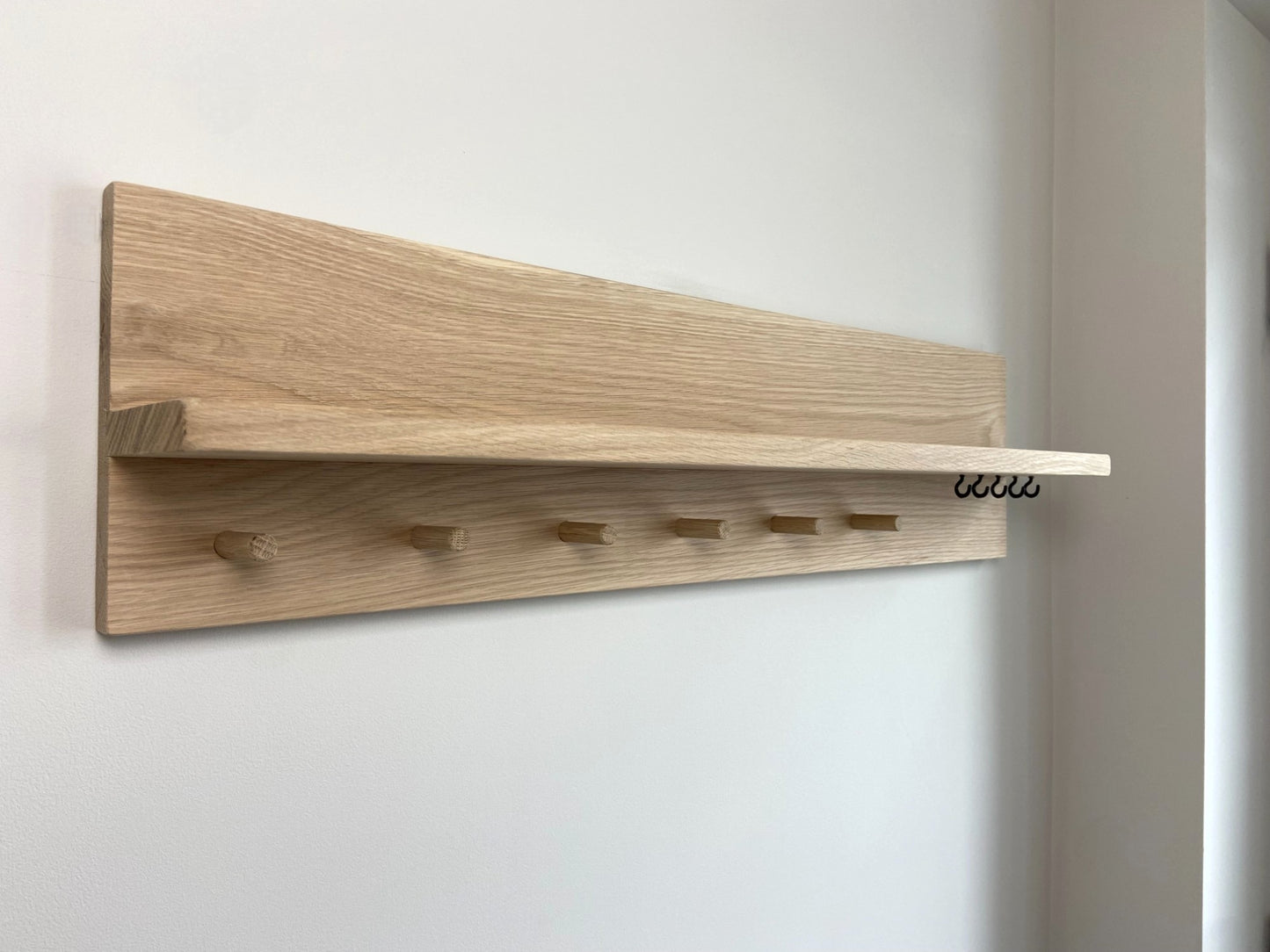 Handcrafted oak organiser shelf clearly showing wooden pegs and hooks  mounted to a wall in an entryway.