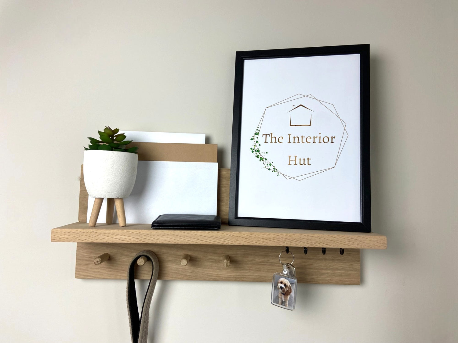 Handcrafted oak organiser shelf with wooden pegs and hooks displaying a plant and picture frame, letters and key. mounted to a wall in a entryway.