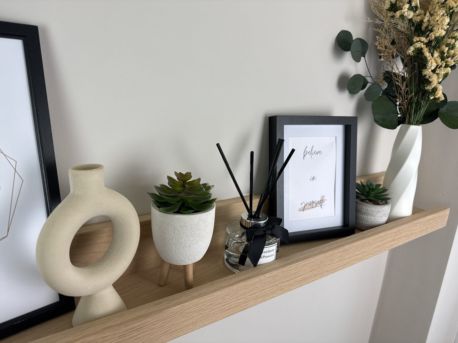 Close-up of the quality craftsmanship of a handmade oak picture shelf, mounted on a plasterboard wall, showcasing a smooth finish and holding photo frames, plants, and small decorative items.