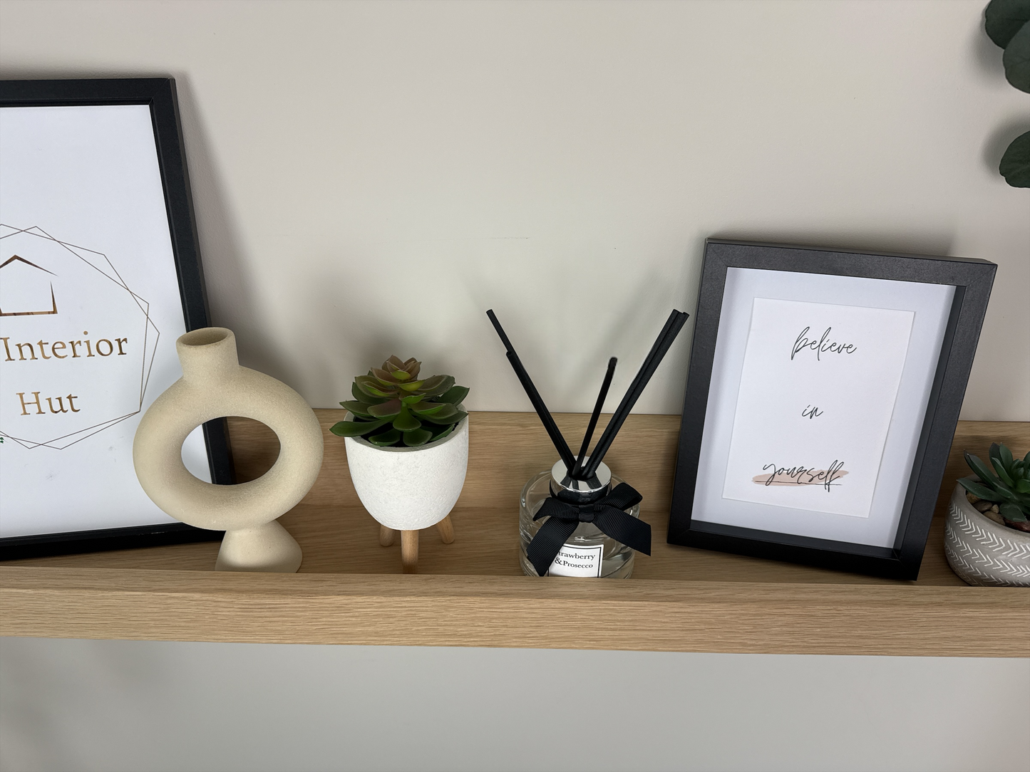 Close-up of the quality craftsmanship of a handmade oak picture shelf, mounted on a plasterboard wall, showcasing a smooth finish and holding photo frames, plants, and small decorative items.