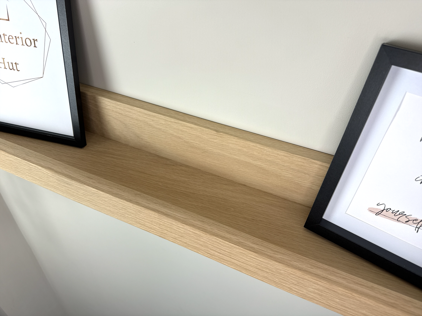 Close-up of the quality craftsmanship of a handmade oak picture shelf, mounted on a plasterboard wall, showcasing a smooth finish and holding photo frames, plants, and small decorative items.