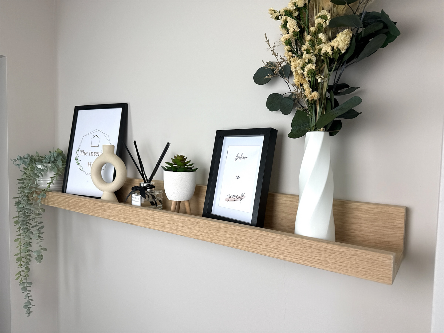 Handmade oak picture shelf, mounted to a plasterboard wall, holding photo frames, plants and small décor items.