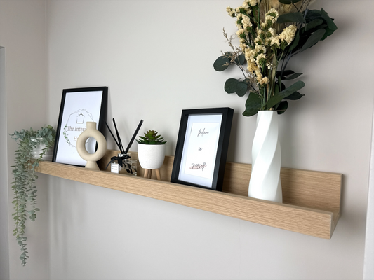 Handmade oak picture shelf, mounted to a plasterboard wall, holding photo frames, plants and small décor items.