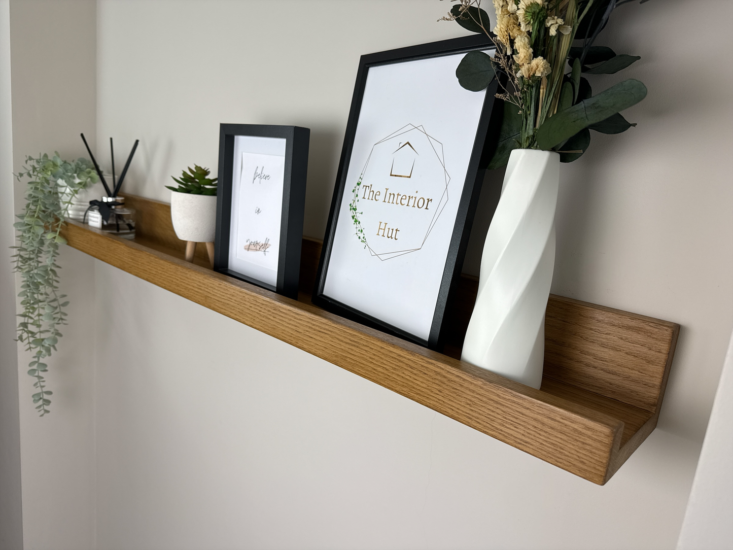 Close-up of the quality craftsmanship of an oak picture shelf with a Rugger Brown wax finish, securely mounted on a plasterboard wall, displaying photo frames and small decorative items.