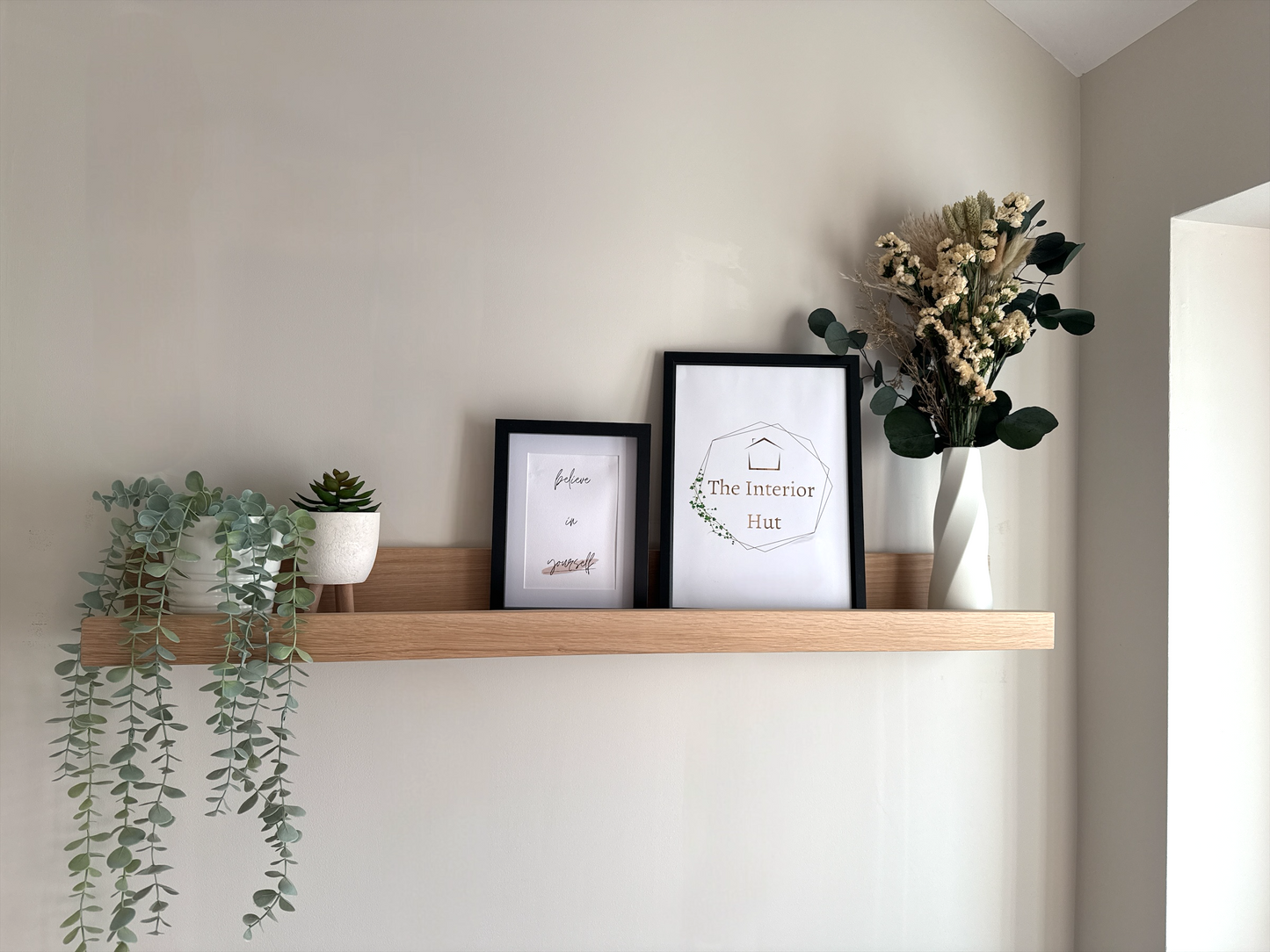 Handmade oak picture shelf, mounted to a plasterboard wall, holding photo frames, plants and small décor items.