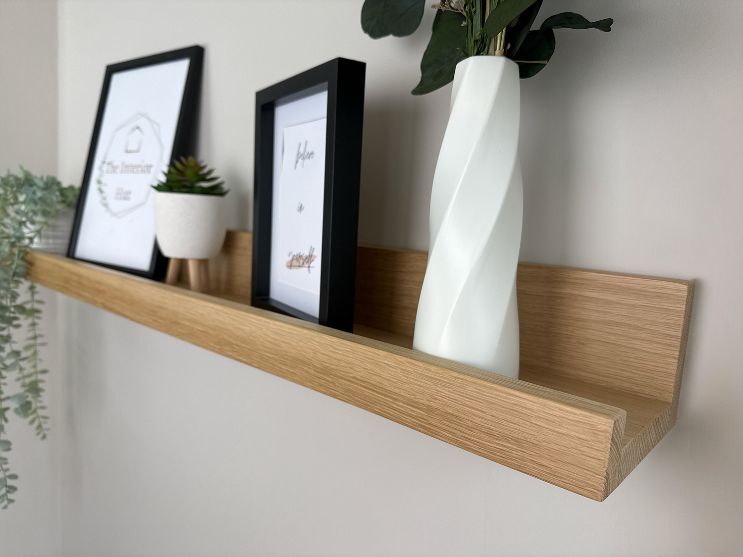 Close-up of the quality craftsmanship of an oak picture shelf with a Light wax finish, securely mounted on a plasterboard wall, displaying photo frames and small decorative items.