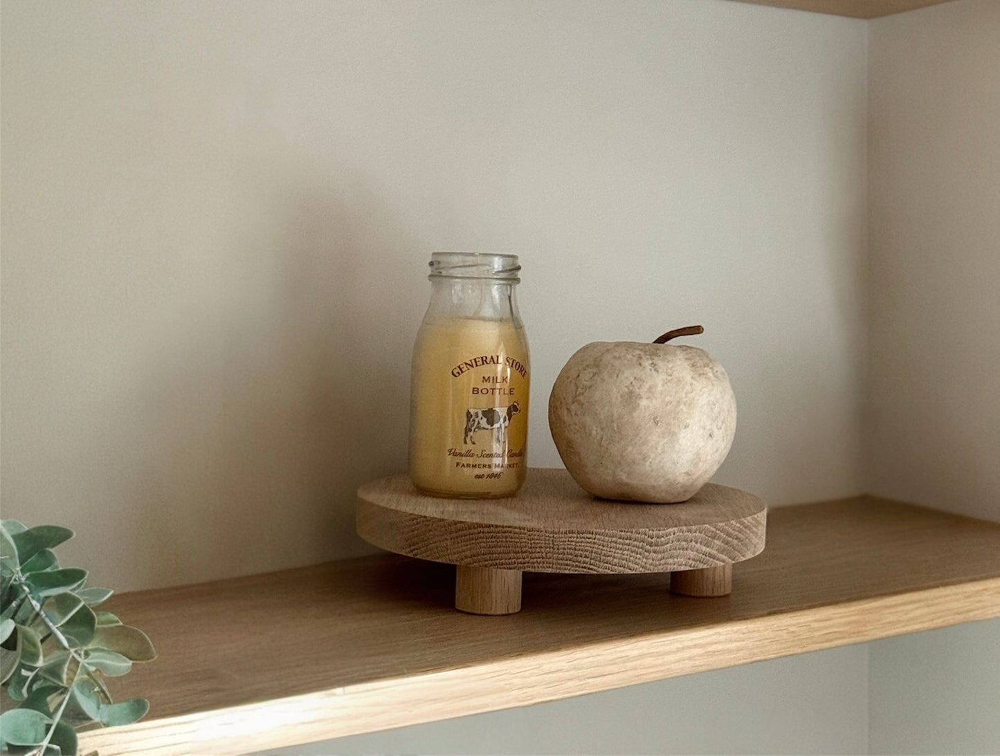Small glass bottle and stone apple on a wooden riser tray against a neutral wall.